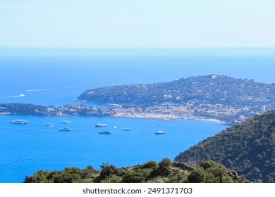 Beautiful coastal view with a vibrant blue sea, a lush green hillside, and a distant island town. The scene includes several boats dotting the water, offering a picturesque landscape under clear sky - Powered by Shutterstock