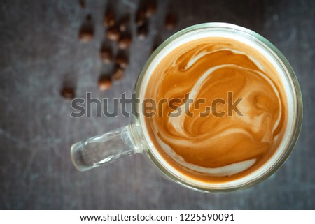 Beautiful coffee milk foam. Coffee with milk in a transparent glass on a dark background top view.