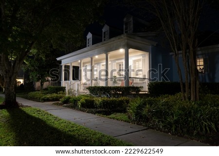 Beautiful Colonial Revival style house with illuminated front porch at night in a suburban neighborhood