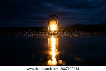 Beautiful colorful illuminated lantern on frozen puddle. The lamp is beautifully reflected in the mirror surface. Cloudy sky.