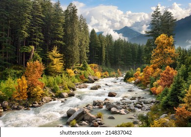 Beautiful colorful landscape with a stream and forest in autumn colors, mountains in the background and blue sky with white clouds