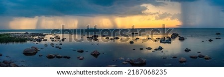 A beautiful colorful midsummer sunset in Northern Estonia (Haabneeme). Storm clouds can be seen on the background of beautiful rocks in a silent calm  blue water.