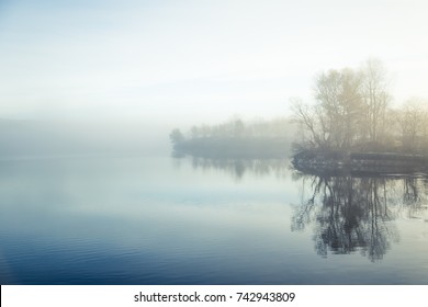 A beautiful, colorful misty morning in Norway at the lake. Tree reflections in the water. Misty autumn landscape. Calm nordic scenery. - Shutterstock ID 742943809