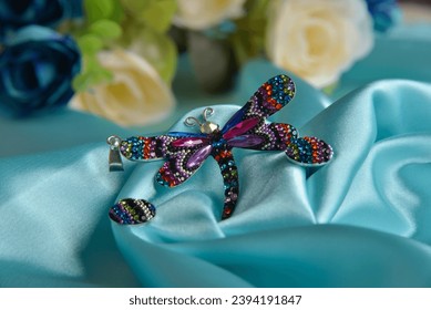 beautiful colorful zircon dragonfly with turquoise blue silk fabric background and flowers in the background - Shutterstock ID 2394191847