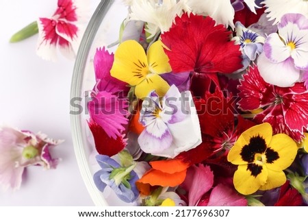 Beautiful colourful yellow violet wite red edible flowers in a small glass bowl on white background copy text space 