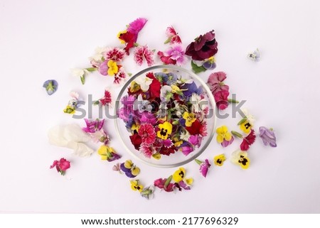 Beautiful colourful yellow violet wite red edible flowers in a small glass bowl on white background copy text space 