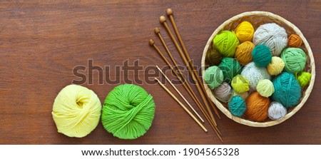 Beautiful composition with accessories for hand knitting: balls of colorful yarn in basket, knitting needles and crochet hooks on wooden background. Needlework and hobby. DIY concept. Flat lay, mockup