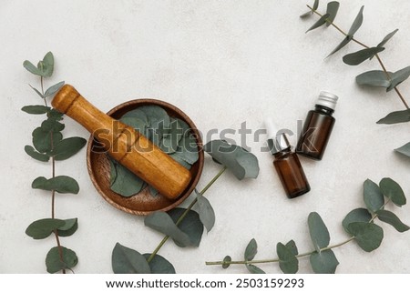 Beautiful composition with bottles of eucalyptus essential oil, wooden mortar and pestle on light background