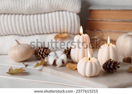 Beautiful composition with candles, pumpkins, books and warm clothes on white wooden background