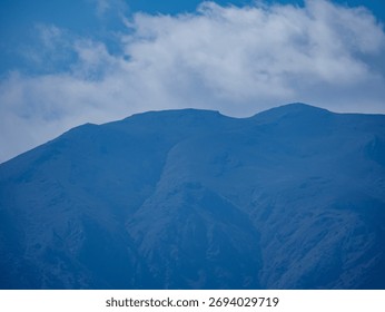 A beautiful composition of a mountain range with a soft layer of white clouds resting above the peaks against a blue sky
