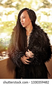 Beautiful confident woman with intricate long braided hair wearing a faux fur coat standing on a balcony looking sideways