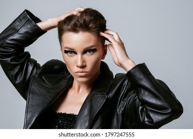 Beautiful Confident Woman With Strong Face, Short Hair, Bold Eyeliner Makeup, Wearing Black Trendy Leather Jacket, Posing On Grey Background. Close Up Studio Fashion, Beauty Portrait