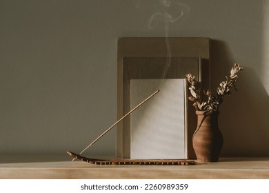 Beautiful contemporary and modern interior - brown ceramic vase with dried eucalyptus, aroma stick, books on wooden shelf at home with daylight. Wellbeing and slow living concept. Empty copy space - Shutterstock ID 2260989359