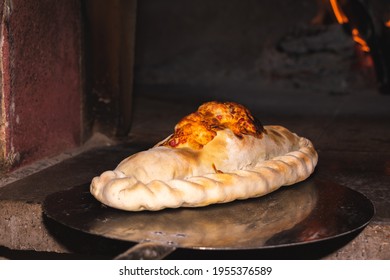 A beautiful cooked calzone being take out from the wooden oven in a baker's shovel - Powered by Shutterstock