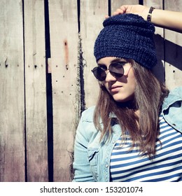 Beautiful Cool Girl In Hat And Sunglasses Against Grunge Wooden Fence, Toned And Noise Added