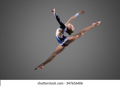 Beautiful cool young fit gymnast woman in blue sportswear dress working out, performing art gymnastics element, jumping, doing split leap in the air, dancing, full length, studio, dark background