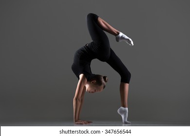 Beautiful cool young fit gymnast athlete woman in sportswear doing art gymnastics, bridge, backward extension acrobatic exercise on one leg, full length, studio image, dark background - Shutterstock ID 347656544