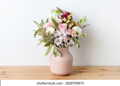 Beautiful cottage style flower arrangement, in a pink vase, on a wooden table. Flower bunch includes Roses, Snapdragons, Ranunculus, Daisy's, Chrysco, Lily of the Incas, Thryp and lush green foliage.  - Shutterstock ID 1828790873