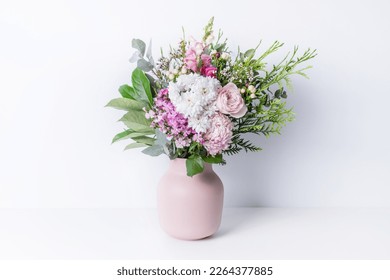 Beautiful cottage style flower arrangement, in a pink vase, on a white table. Flower bunch include Rose, Snapdragon, Ranunculus, Daisy's, Sweet William, Chrysanthemum and lush green foliage.  - Shutterstock ID 2264377885