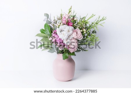 Beautiful cottage style flower arrangement, in a pink vase, on a white table. Flower bunch include Rose, Snapdragon, Ranunculus, Daisy's, Sweet William, Chrysanthemum and lush green foliage. 
