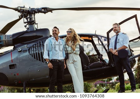Beautiful couple alighted from a private helicopter and looking at a view with pilot standing by. Couple standing by a private aircraft with pilot.