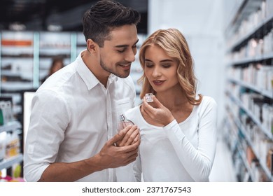 Hermosa pareja está eligiendo perfumes y sonriendo mientras hace compras en el centro comercial