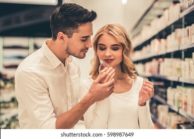 Beautiful couple is choosing perfumes and smiling while doing shopping in the mall