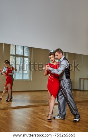 beautiful couple dancing tango. young woman in red dress and man in suit practicing in dancing studio mirror room. copy space.