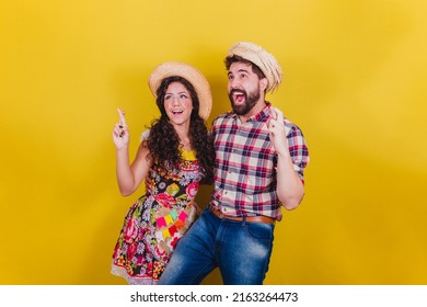 Beautiful couple dressed in typical clothes for a Festa Junina. Arraia de Sao Joao. Fingers crossed, cheering, wishing, luck concept.