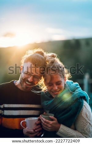 Beautiful couple drinking coffee or tea on the modern terrace in mountains. Happy couple holding cups and making plans for the day while enjoying each other. Romantic concept. Copy space.