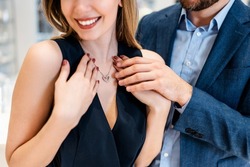 Beautiful Couple Enjoying In Shopping At Modern Jewelry Store. Young Woman Try It Out Gorgeous Necklace And Earrings. Selective Focus On Necklace With Pendant. Fashion Style And Elegance Concept.