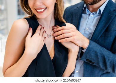 Beautiful couple enjoying in shopping at modern jewelry store. Young woman try it out gorgeous necklace and earrings. Selective focus on necklace with pendant. Fashion style and elegance concept. - Shutterstock ID 2154603267