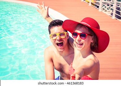 Beautiful couple having fun taking selfie at swimming pool  - Cheerful friends enjoy mobile photo camera using stick on sunny day  - Concept of happy moments on board of touristic ship - Focus on male - Powered by Shutterstock