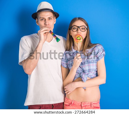Beautiful couple having a fun together. Posing on blue background with lollipop.