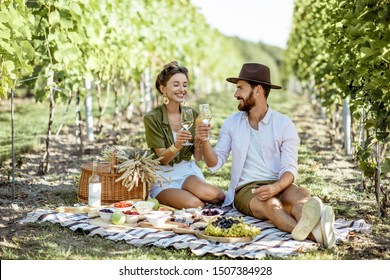 Beautiful couple having romantic breakfast with lots of tasty food and wine, sitting together on the picnic blanket at the vineyard on a sunny morning - Powered by Shutterstock