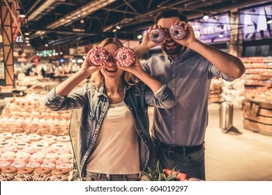 Beautiful couple is holding donuts and smiling while doing shopping at the supermarket