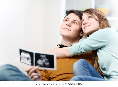 Beautiful couple imagines the future of their unborn child with ultrasound pictures in hands - Powered by Shutterstock