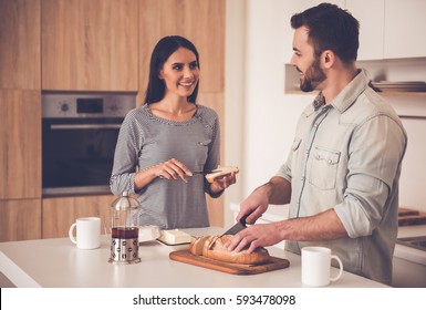 Beautiful couple in kitchen. Handsome man is cutting bread while his wife is doing sandwiches, both are smiling - Powered by Shutterstock