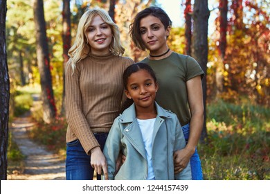 A Beautiful Couple Of Lesbian Ladies Posing In The Autumn Park With Their Adopted Teenage Daughter. The Happy Young Family Standing, Looking At The Camera, Smiling. The Girls Wearing Casual Outfit.