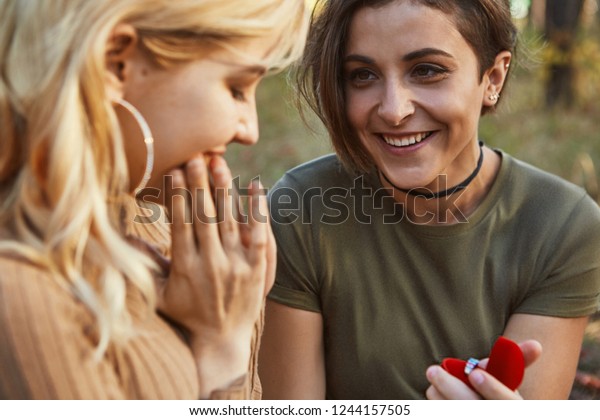 公園に座っているレズビアンの女性の美しいカップル 金髪の彼女に箱の中の指輪を渡すブルネットの女の子 その金髪の女性は 恋人から意味のある贈り物を受け取って嬉しい の写真素材 今すぐ編集