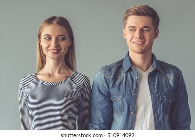 Beautiful couple is looking at each other and smiling while standing straight on gray background