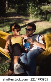 Beautiful couple looking at the polaroid picture while sitting on the yellow hammock in the park - Shutterstock ID 2214993935