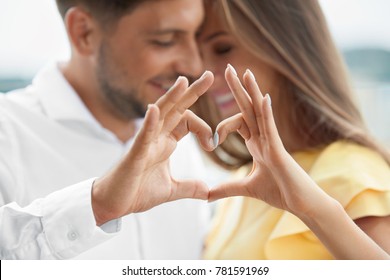 Beautiful Couple In Love Making Heart With Hands. Happy Smiling Young People Hugging, Showing Heart Shape With Hands And Enjoying Each Other Outdoors. Romantic Relationships. High Quality Image.