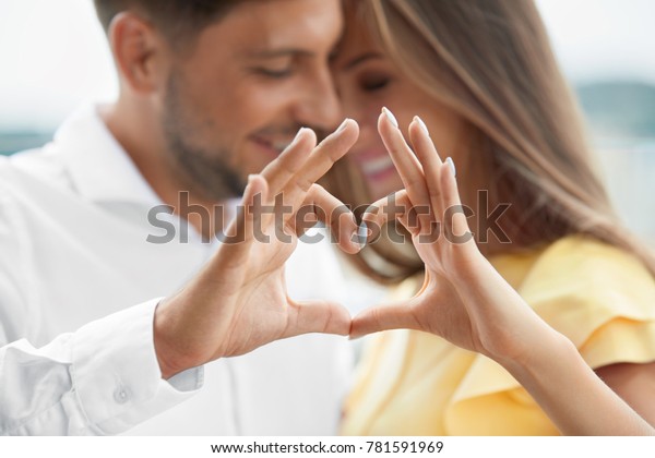 Beautiful Couple In Love Making Heart With Hands.\
Happy Smiling Young People Hugging, Showing Heart Shape With Hands\
And Enjoying Each Other Outdoors. Romantic Relationships. High\
Quality Image.