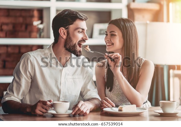 愛する美しい夫婦はカフェで座り コーヒーを飲み チーズケーキを食べている 若い女が男に餌をやっている お互いを静かに見つめ合う の写真素材 今すぐ編集