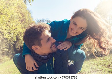 Beautiful couple of lovers joking outdoors in the park and enjoying their time together , with trees around , feeling free in vacation and playing piggyback laughing and having a good time