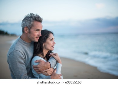 Beautiful couple on the beach at sunset. The man tightens the woman in his arms and they look at the horizon