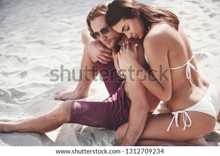 A beautiful couple relaxing on the sandy beach, wearing bathing clothes. Romantic atmosphere.