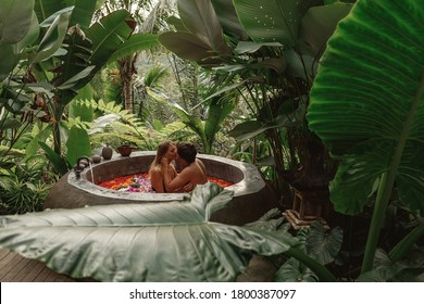 Beautiful couple resting in hotel spa. Woman and man relaxing in bath with tropical flowers outdoor at luxury hotel resort in the jungle