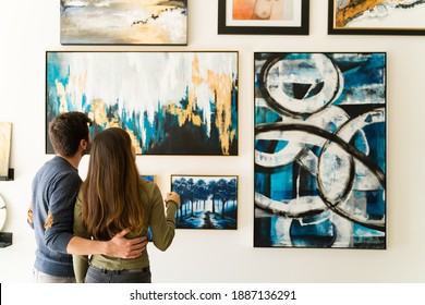 Beautiful couple seen from behind is hugging while admiring the paintings and colorful canvases hanging on the wall of the gallery  - Shutterstock ID 1887136291